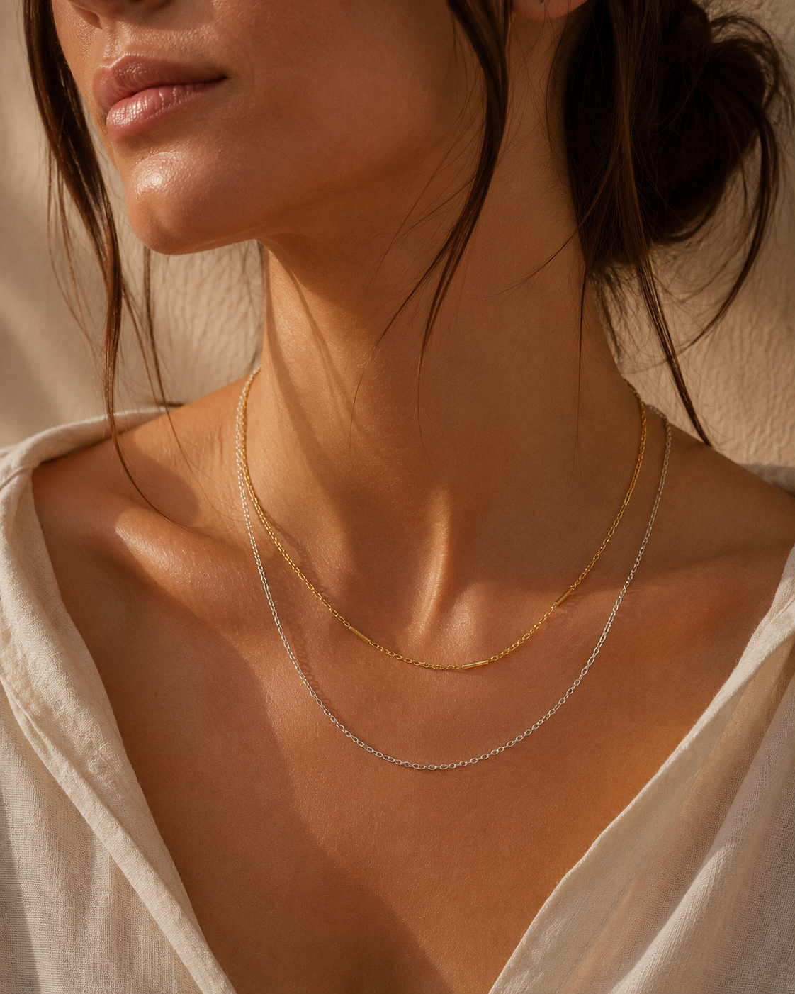 Model layers the gold and silver Filo NECKLACE chains together at the neckline, paired with a cream linen shirt in warm sunlight.