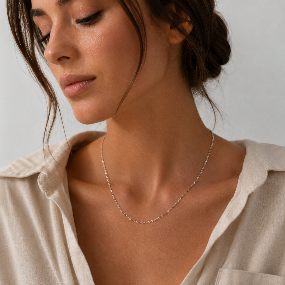Model wears the silver Filo NECKLACE close to the neckline, paired with a cream linen shirt in soft natural light.