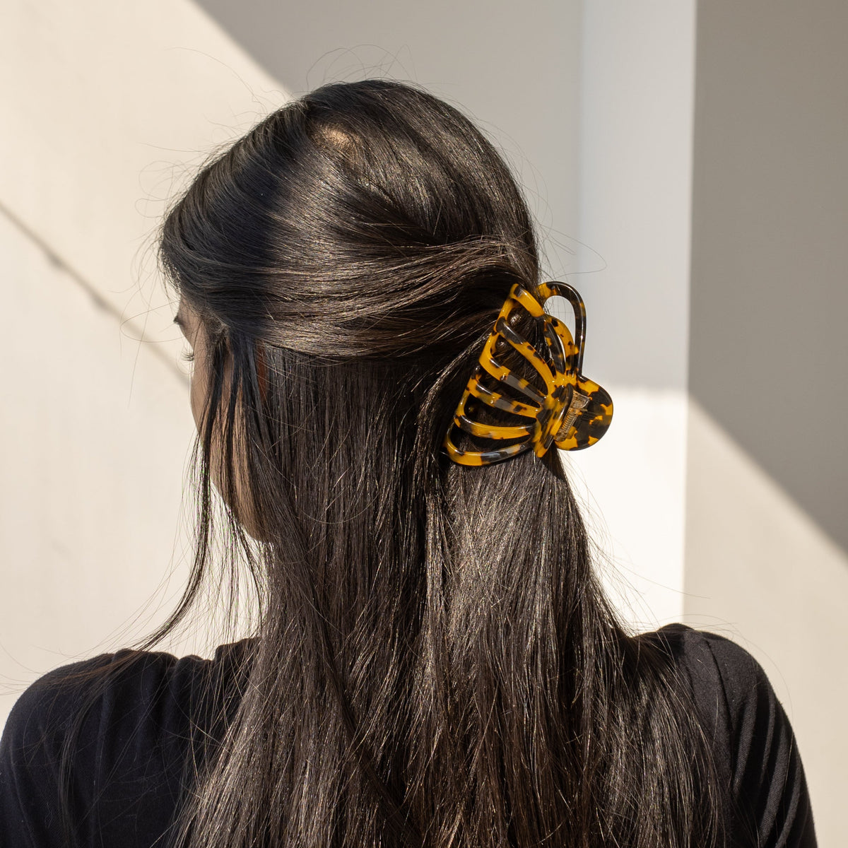 Forget About Me HAIR CLIP's tortoiseshell claw clip worn in a half-up hairstyle, clipped into dark hair in soft sunlight.
