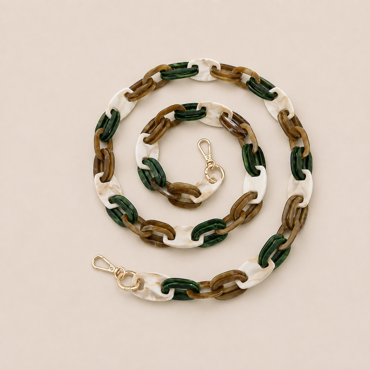 Folie à Trois Frost long phone chain in white marbled, dark green and brown links with gold clasps, coiled on a cream background.