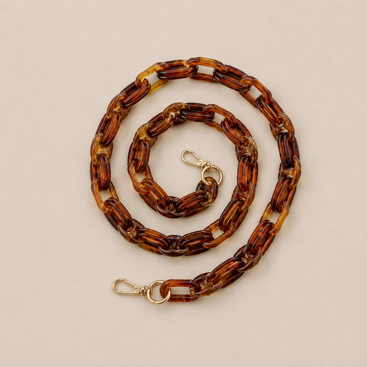 Folie à Trois Frost long phone chain in tortoiseshell links with gold clasps, coiled on a cream background.
