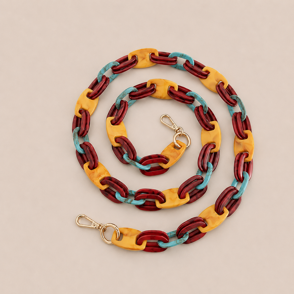 Folie à Trois Frost long phone chain in burgundy, mustard and turquoise links with gold clasps, coiled on a cream background.