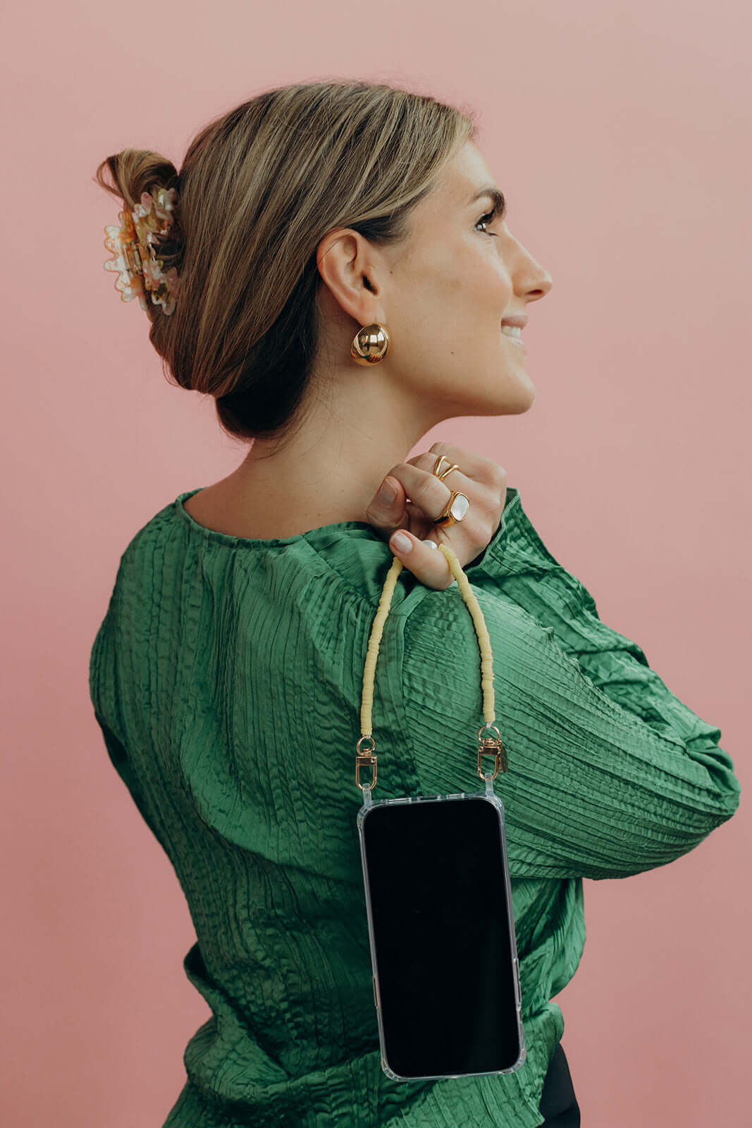 Woman in a green blouse with a floral Funky HAIR CLIP in her bun, carrying a phone on a strap over her shoulder, pink wall.