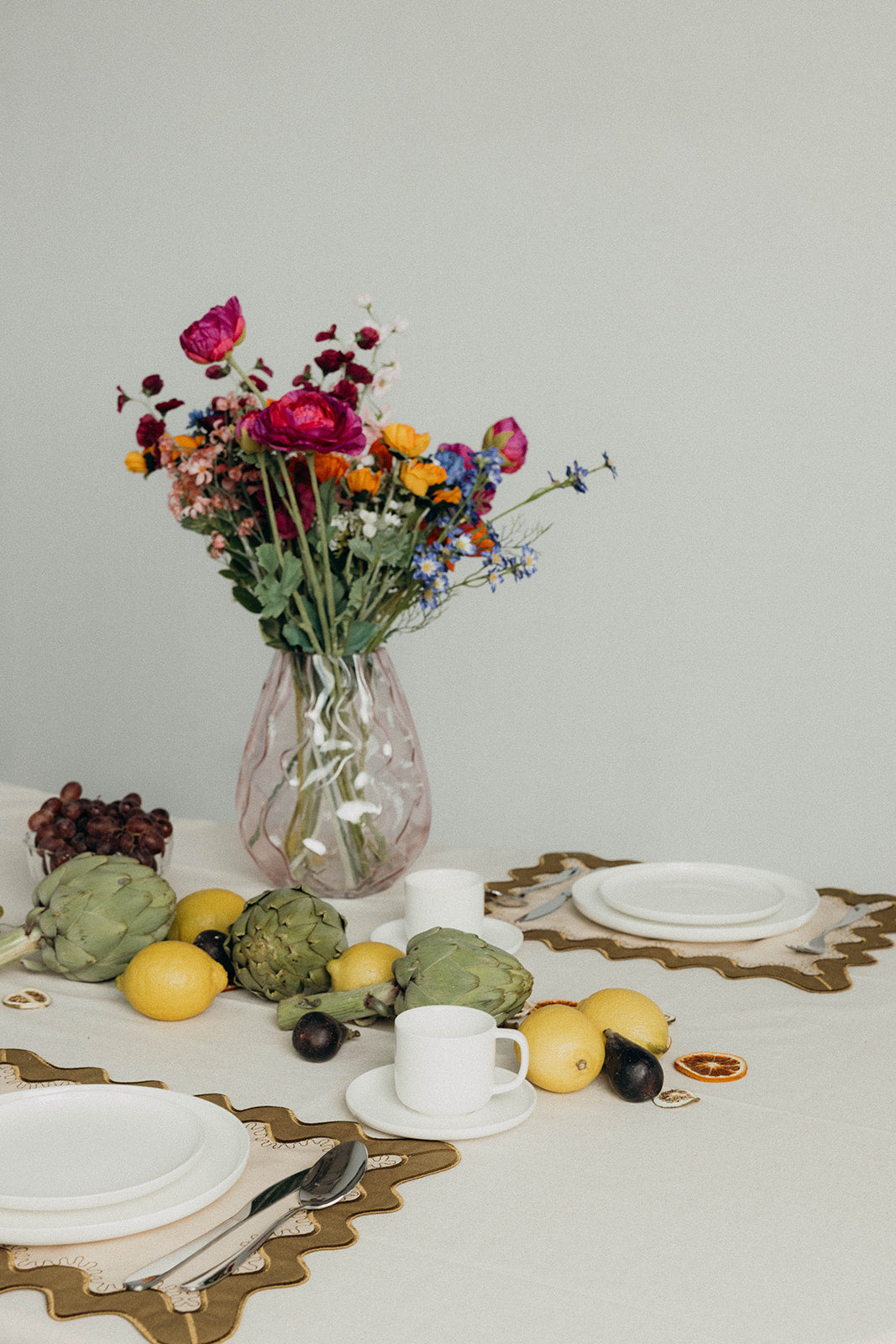 Styled brunch table with fresh flowers, fruit, and white plates set on the olive Gisèle Scallop placemat with embroidered edging.