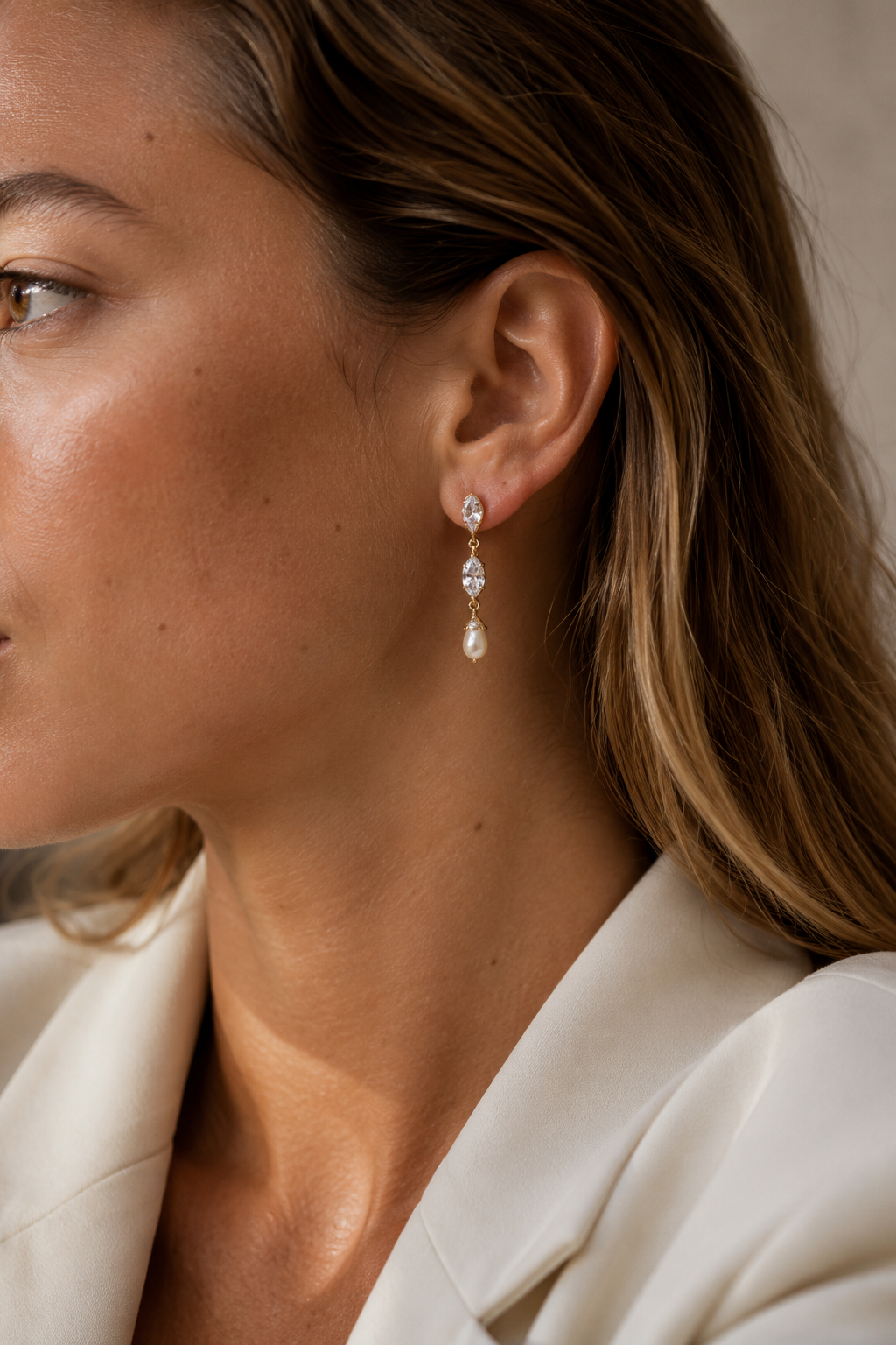 Close-up of a model in a cream blazer wearing the gold Glint EARRINGS, two marquise-cut white zirconia stones linked in a row.