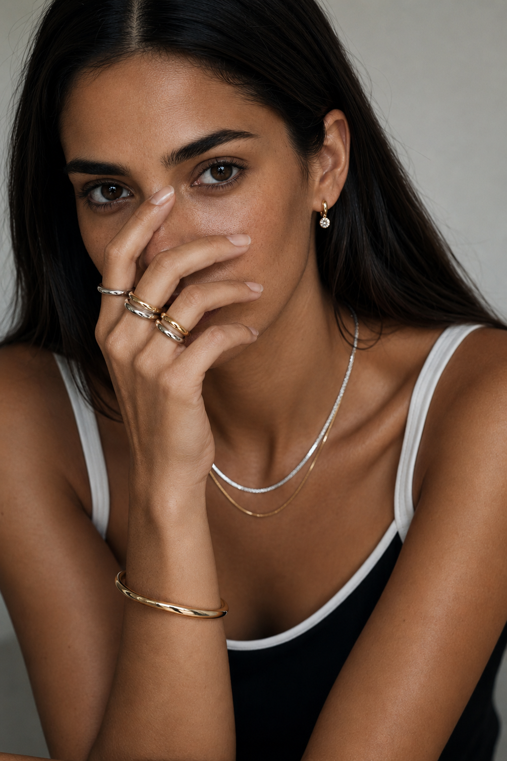 Model wears the gold Halcyon EARRINGS drop, layered with stacked rings, a twisted bangle and fine necklaces.