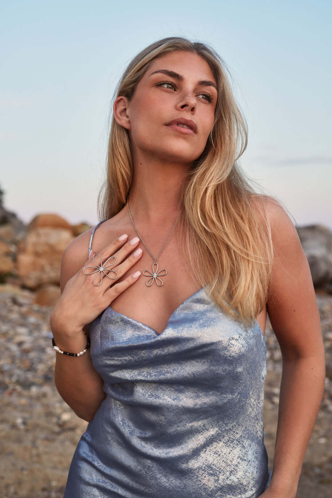 Harlyn BRACELET worn on the wrist, model touching her shoulder in a silver dress, layered with a flower necklace.
