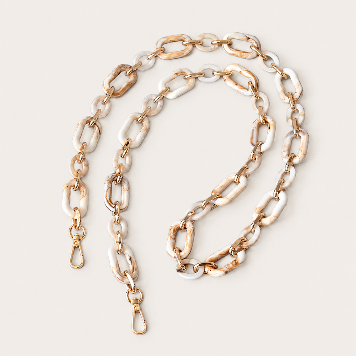The Hazel LONG PHONE CHAIN in cream-and-tan marbled rectangular-link acrylic with gold-tone clasp ends, coiled on a beige background.