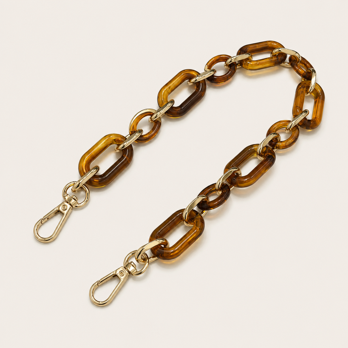 The Hazel SHORT PHONE CHAIN in amber tortoiseshell rectangular-link acrylic with gold-tone lobster clasp ends, fanned on a beige background.