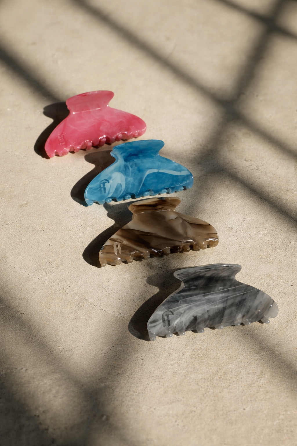 Ice Queen HAIR CLIP's pink, blue, brown and grey marbled claw clips laid out diagonally on sunlit concrete.