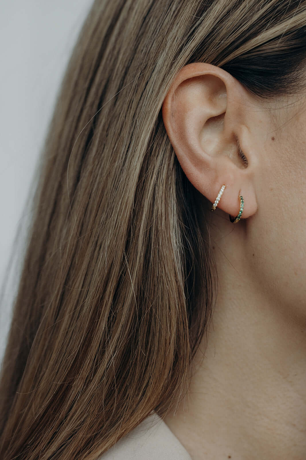 In a Dream Earrings worn on the ear, a pearl-white pave hoop stacked above a green crystal hoop along the lobe.