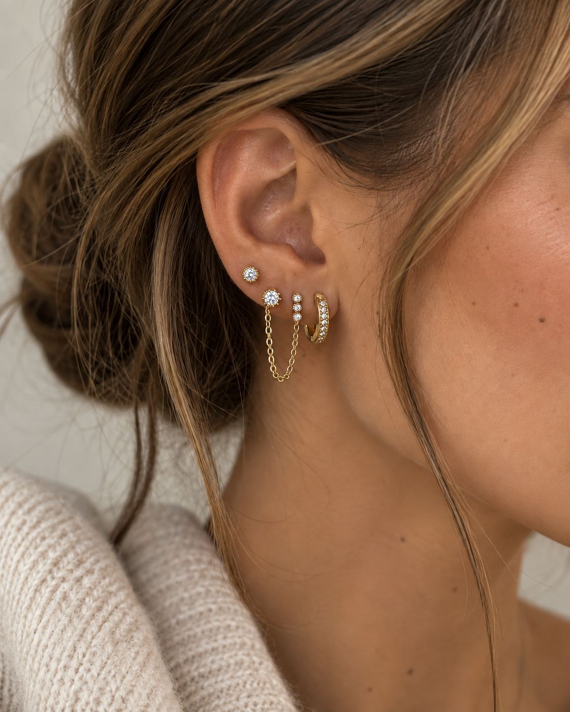 Model's ear wearing the gold Folie à Trois Ines SET: a bezel stud, a chain-linked drop earring and a pavé huggie hoop stacked together.