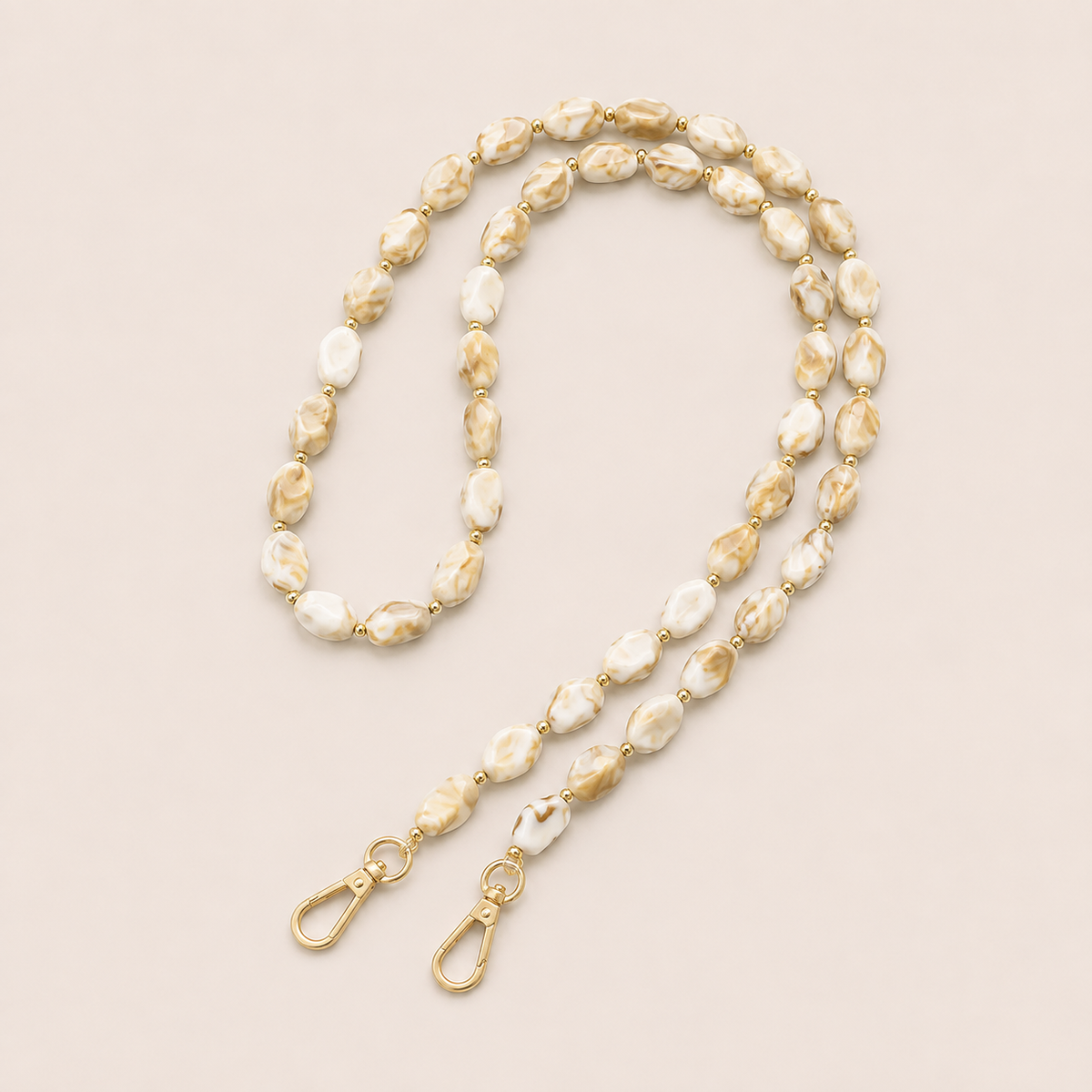 Folie à Trois Isolde long phone chain in cream and tan marbled beads with gold accent beads and gold lobster clasps, laid flat on a cream background.