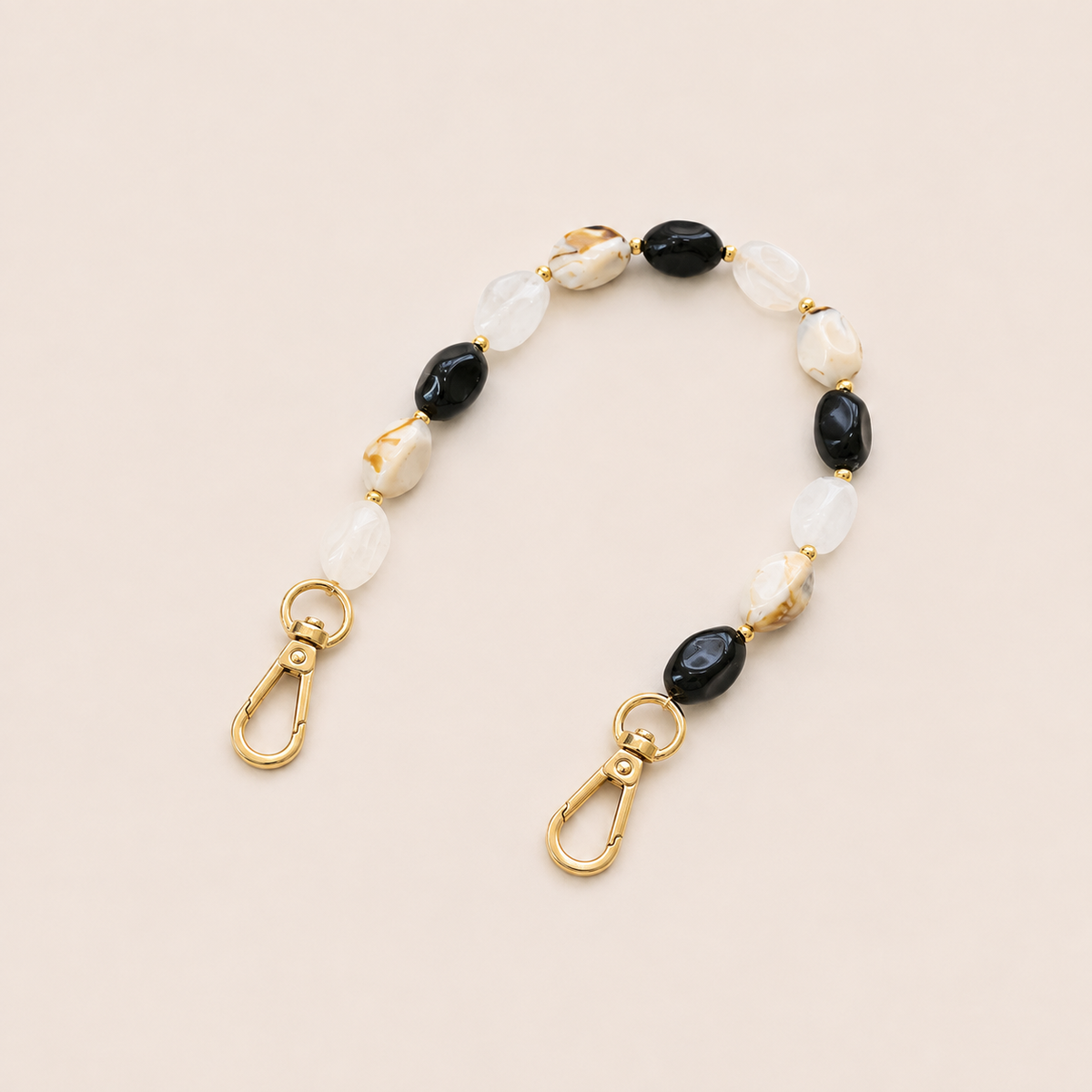 Folie à Trois Isolde short phone chain in black, cream and marbled tan beads with gold accent beads and gold lobster clasps, laid flat on a cream background.