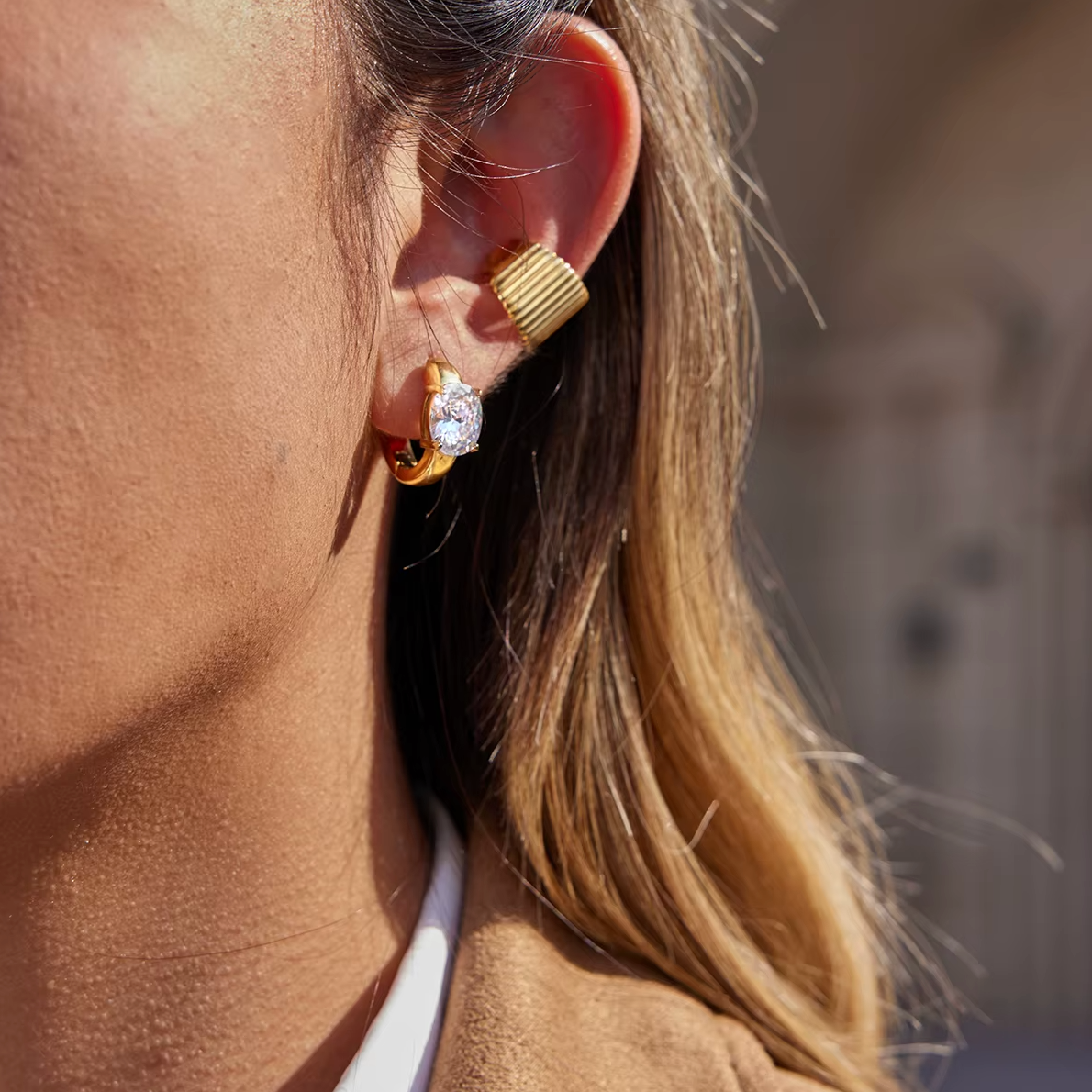 A model wears a gold Ivette EAR CUFF with a fluted, ribbed texture stacked above a hoop with a round stone.
