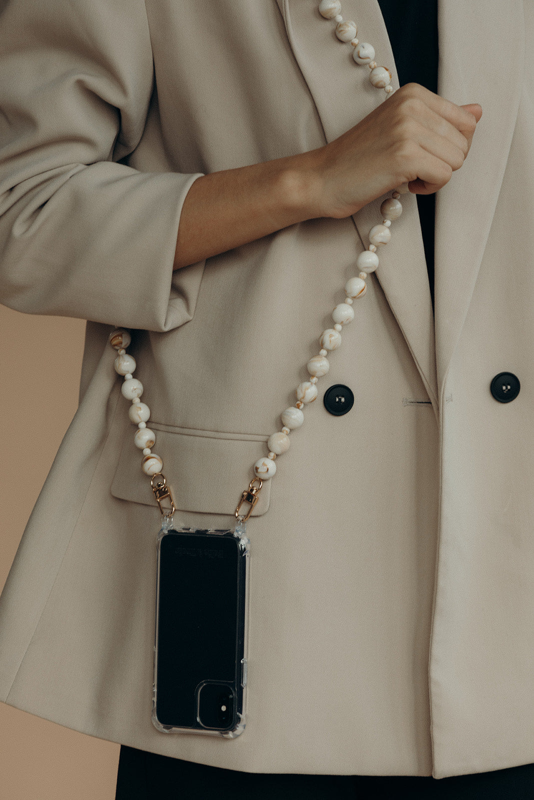 Close-up of a cream and gold marbled bead phone chain with a phone tucked into the pocket of a beige blazer.