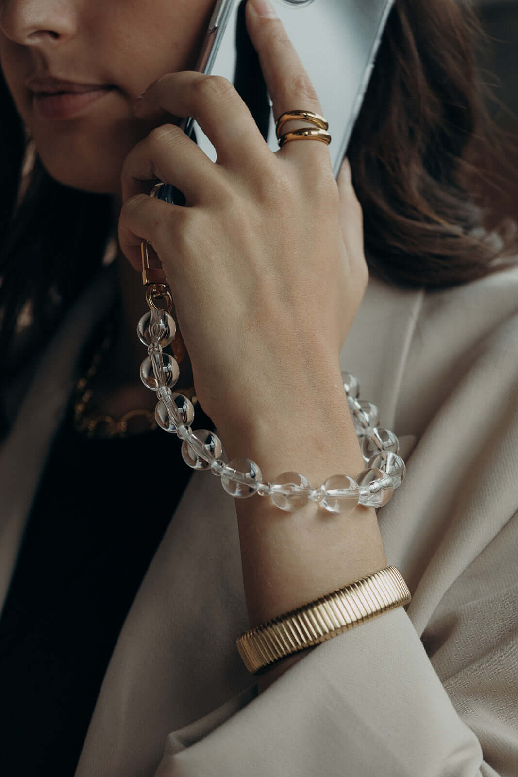 Close-up of a woman on the phone, wearing a clear glass bead bracelet on her wrist along with a ribbed gold bangle.