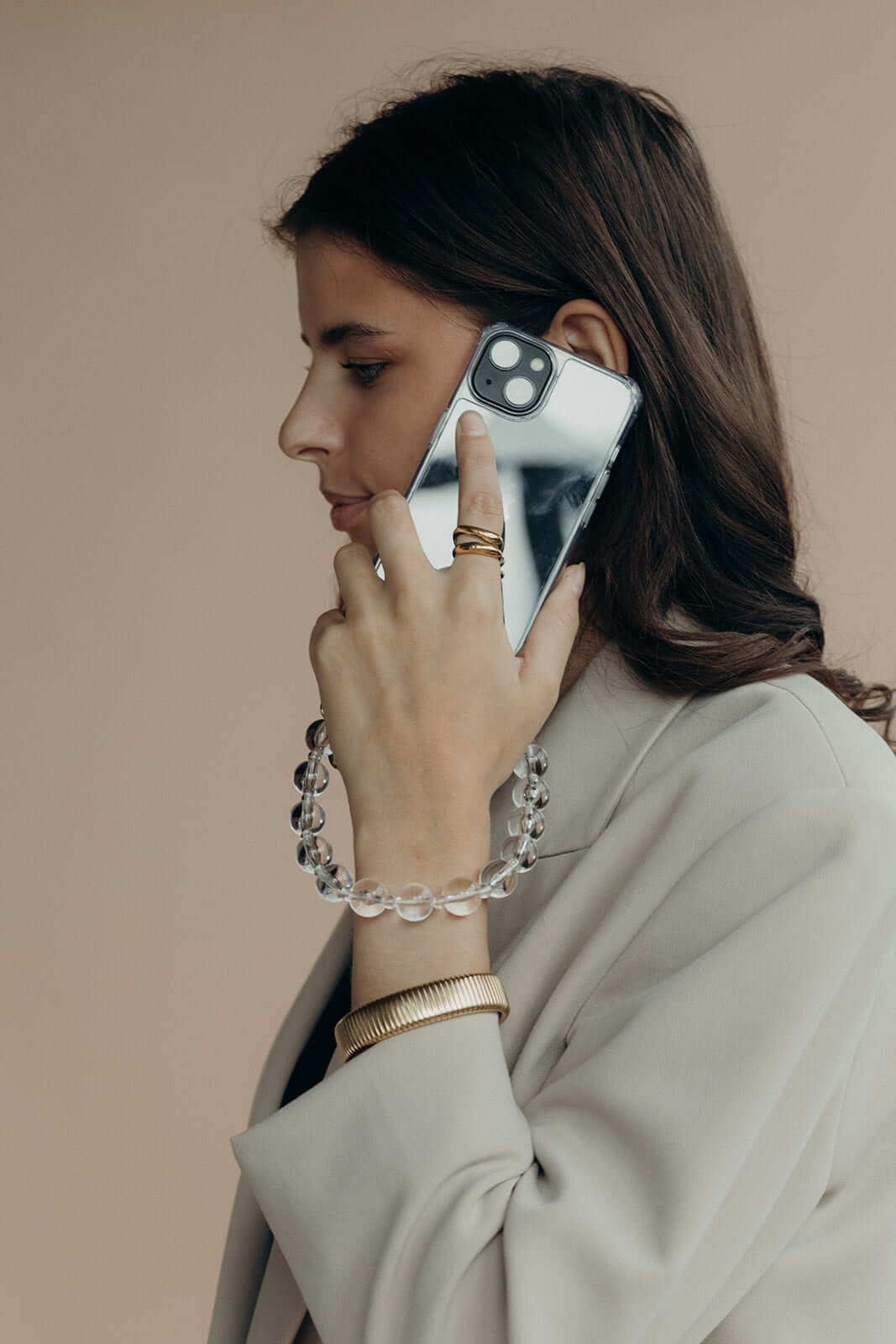 A woman on the phone, wearing a clear glass bead bracelet on her wrist over a light grey blazer sleeve.