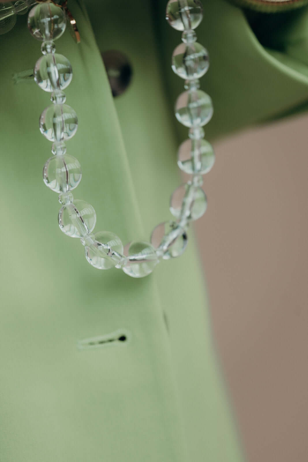 Close-up of clear glass beads on a phone strap, resting against a sage green blazer pocket.