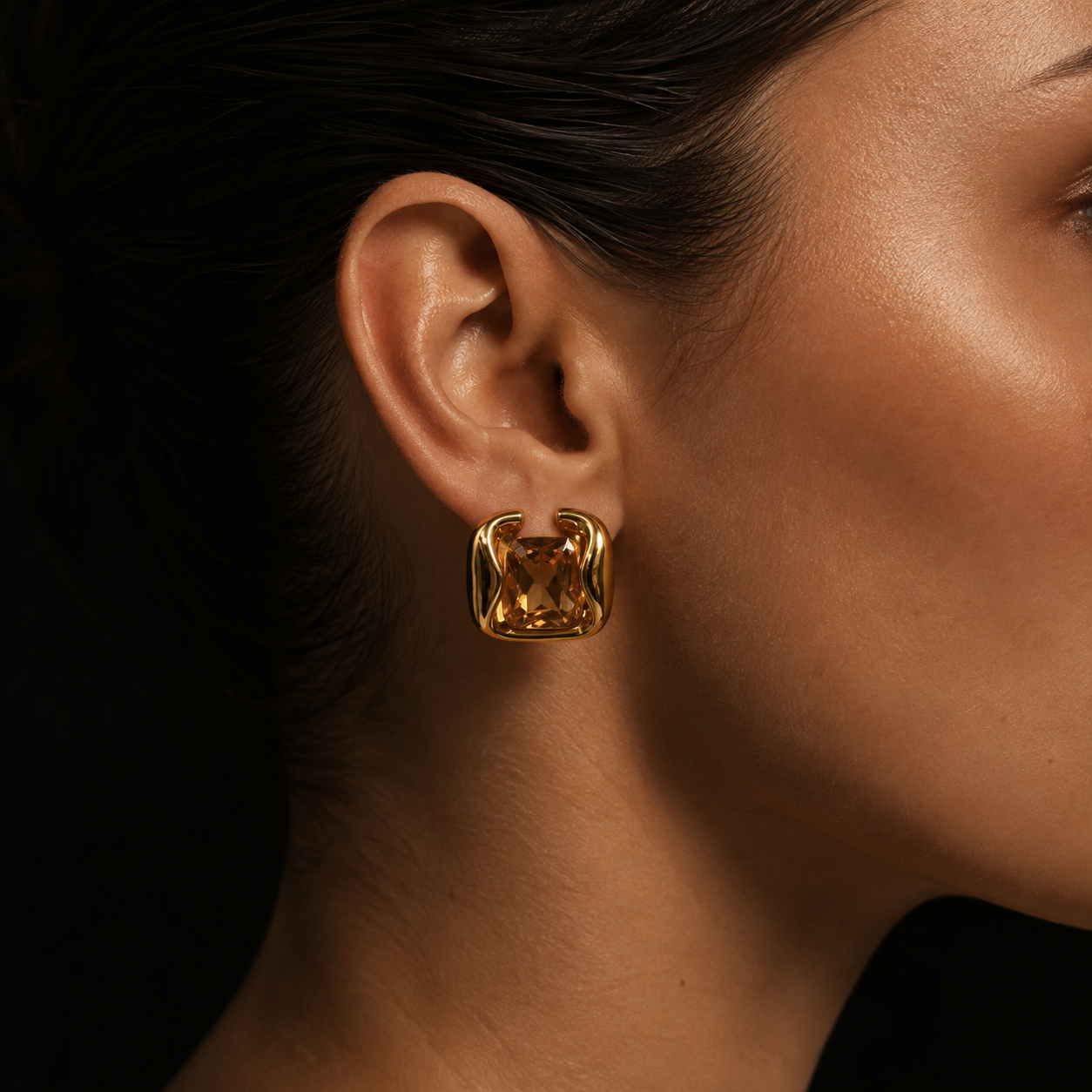 Close-up on the ear of the gold Kaleidoscope EARRINGS, a large champagne-toned stone gripped in a swirled sculptural frame.