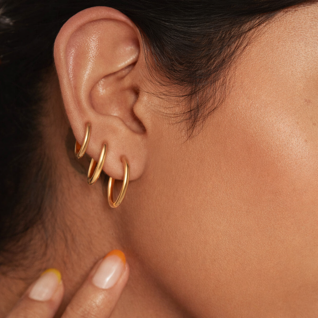 Worn stacked along the ear, Keep The Base Earrings layer three gold huggie hoops of graduated sizes.
