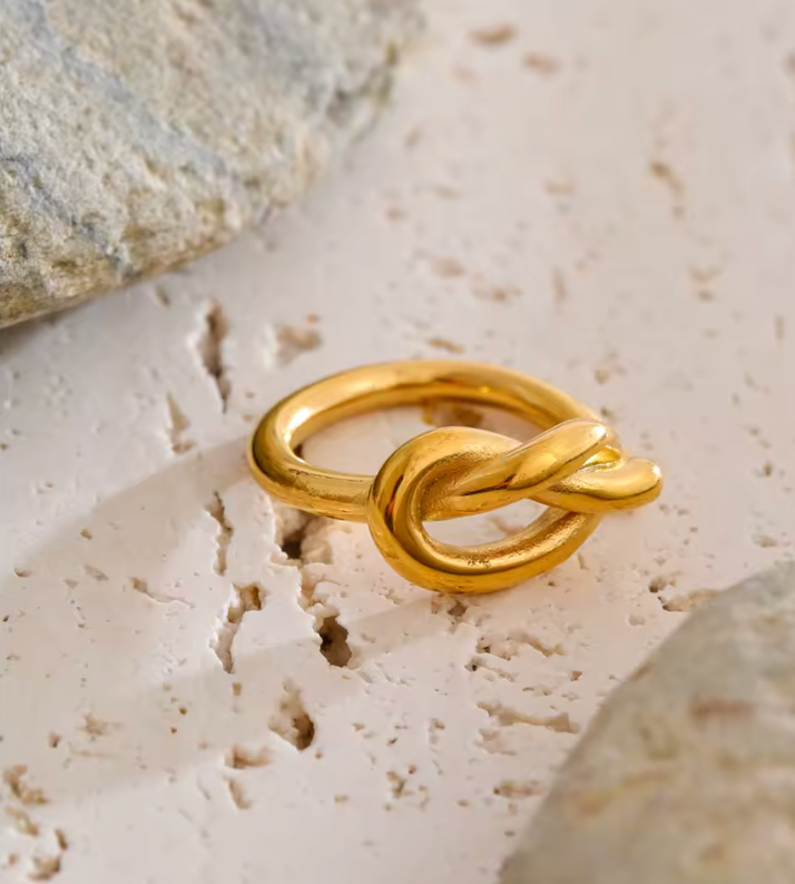 Gold Knotted RING with its sculpted knot detail resting on light stone, textured rock visible in the background.