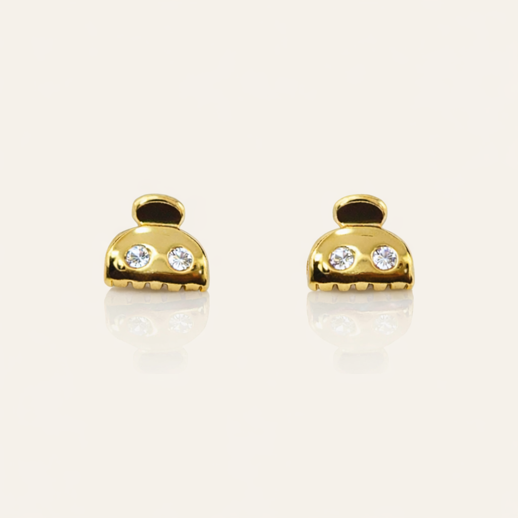 Lay It On Me Earrings take the shape of tiny gold handbags, each set with two round clear stones and a fringed base.