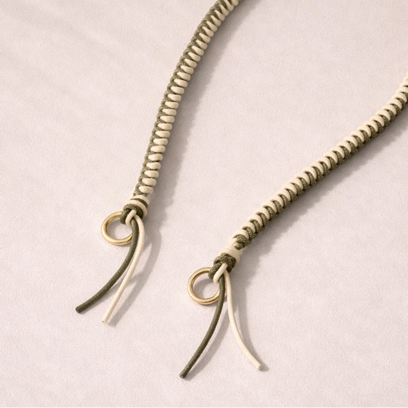 White and olive two-tone braided Layover strap, close-up of the knotted gold ring and fringe end.