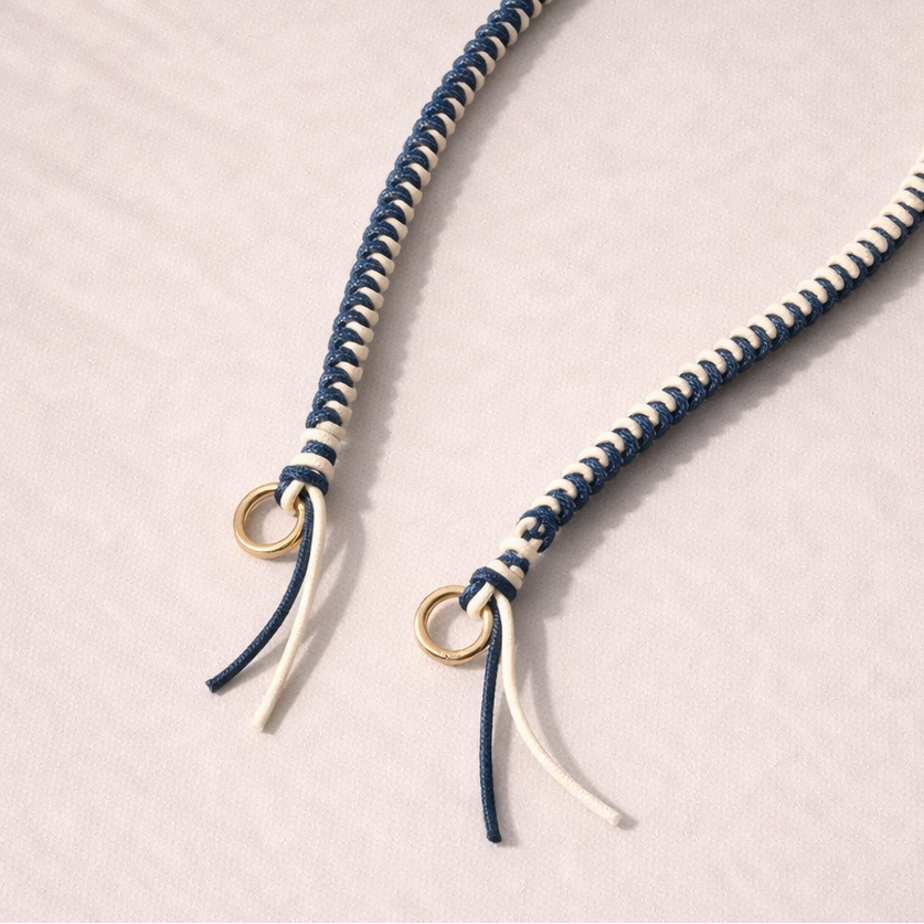 Navy and white two-tone braided Layover strap, close-up of the knotted gold ring and fringe end.