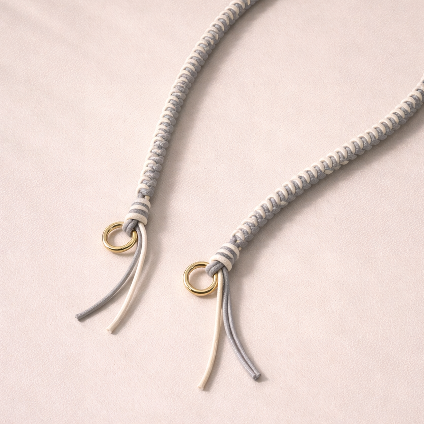 Gray and white two-tone braided Layover strap, close-up of the knotted gold ring and fringe end.