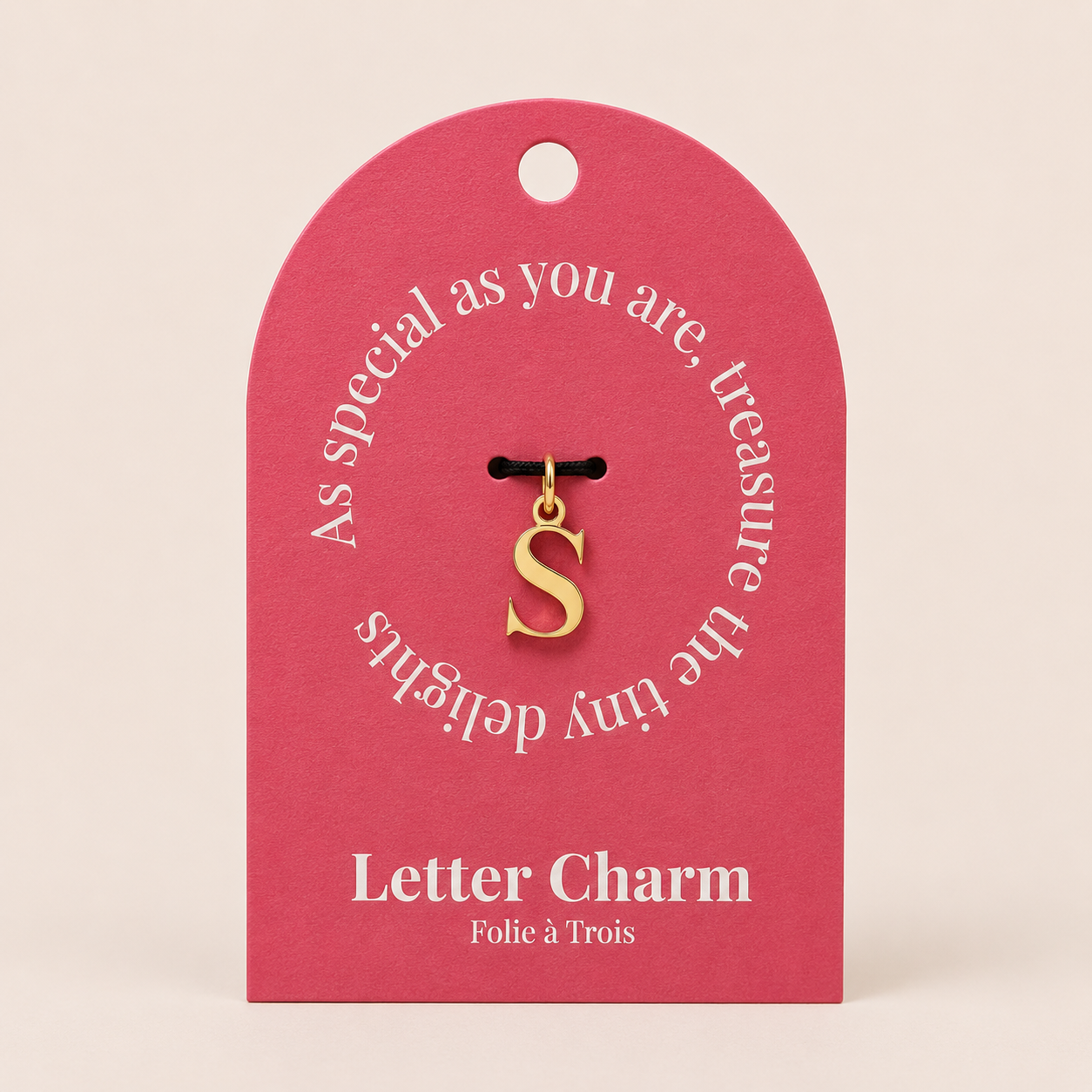 The Letter CHARM in lowercase s on a coral Letter Charm gift tag with Folie a Trois branding, hung from a black cord.