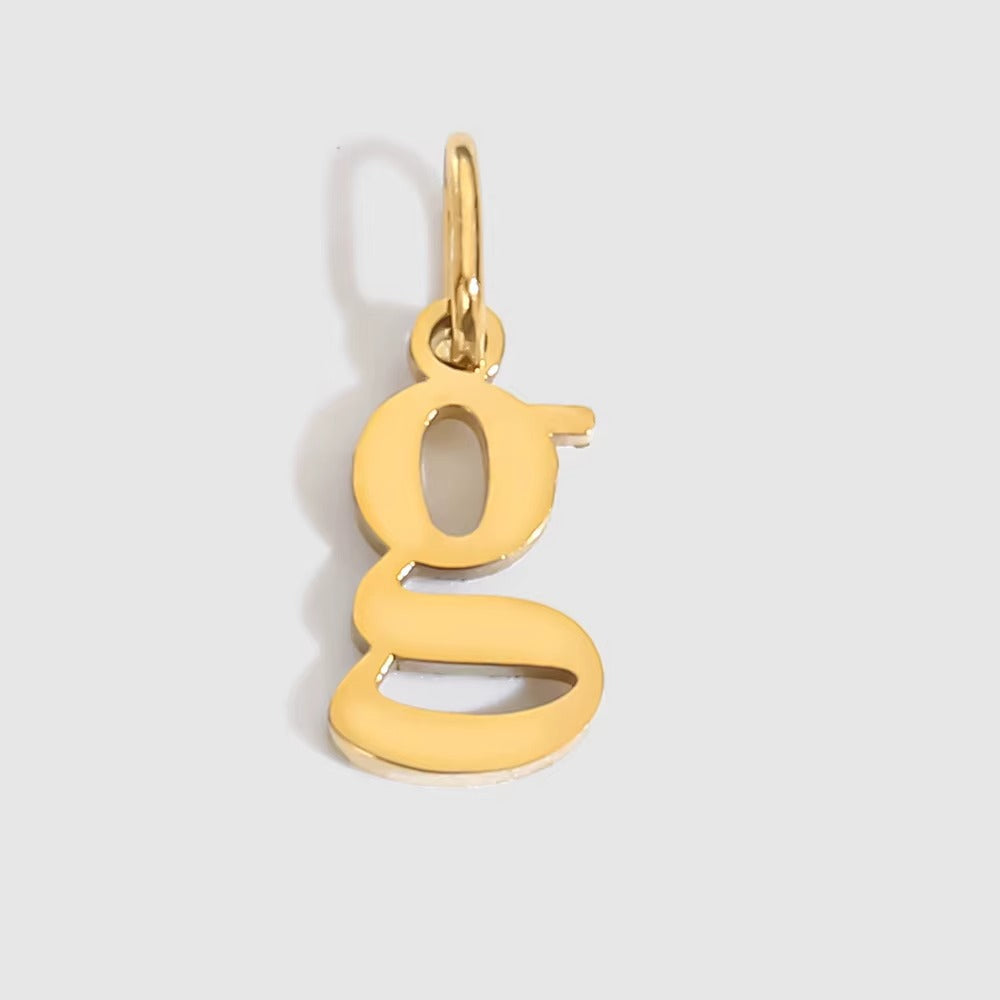 The Letter CHARM in lowercase g, a polished gold pendant in a serif g shape, shown in close-up on a light grey background.