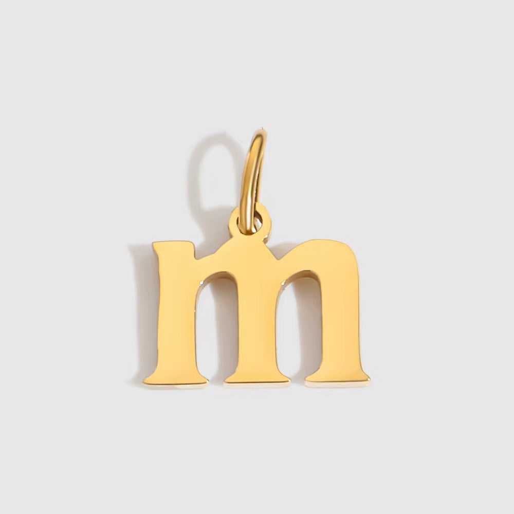 The Letter CHARM in lowercase m, a polished gold pendant in a serif m shape, shown in close-up on a light grey background.