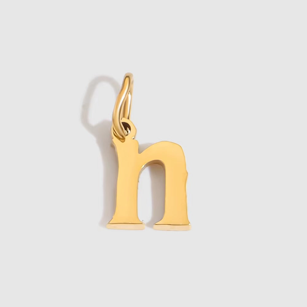 The Letter CHARM in lowercase n, a polished gold pendant in a serif n shape, shown in close-up on a light grey background.