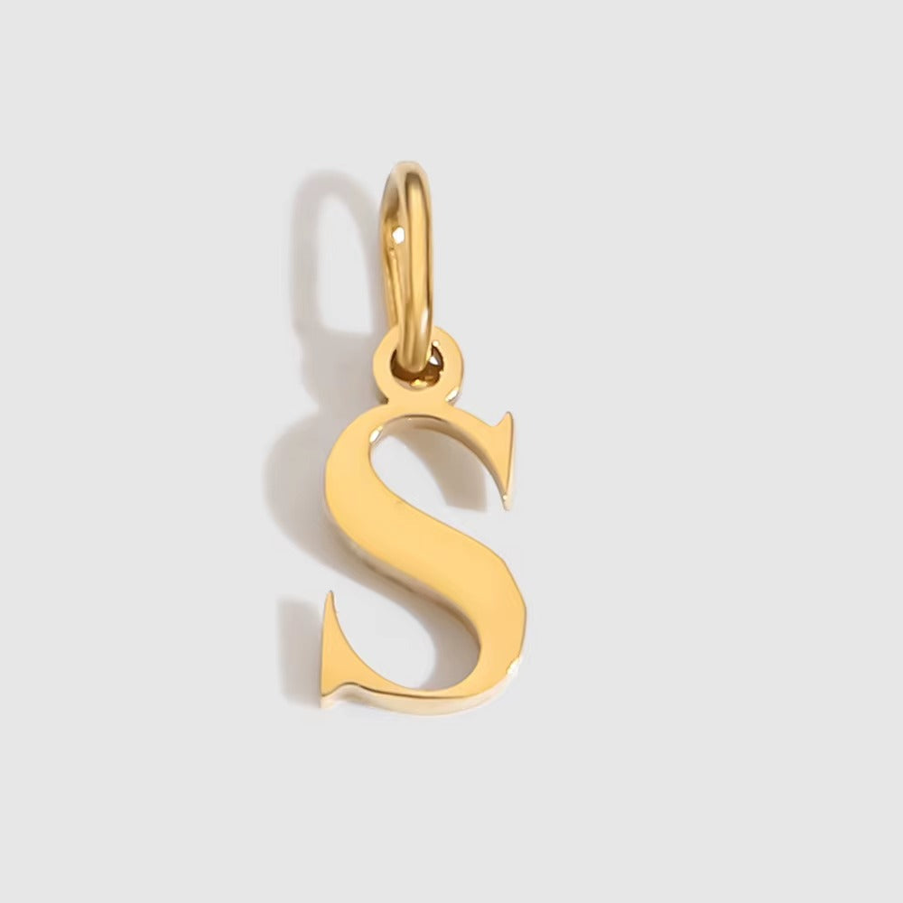 The Letter CHARM in lowercase s, a polished gold pendant in a serif s shape, shown in close-up on a light grey background.