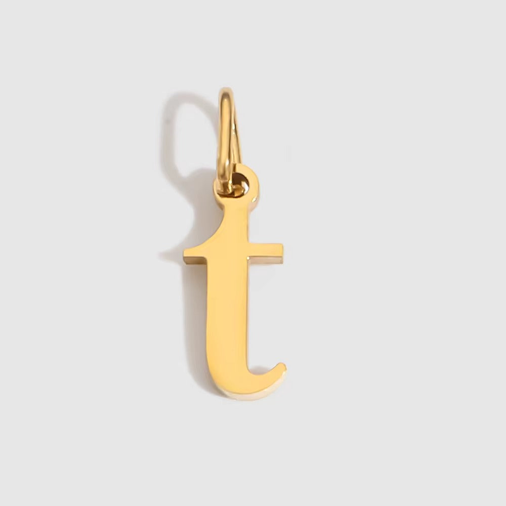 The Letter CHARM in lowercase t, a polished gold pendant in a serif t shape, shown in close-up on a light grey background.