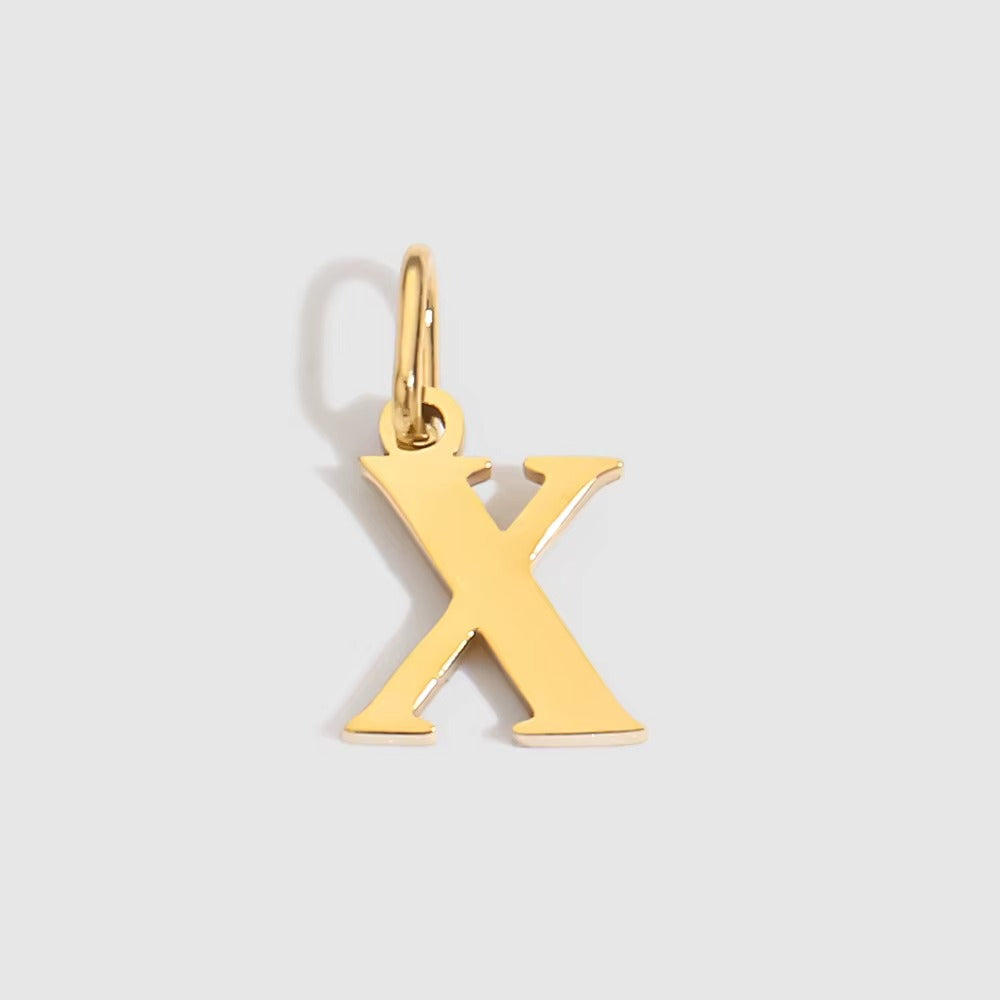 The Letter CHARM in lowercase x, a polished gold pendant in a serif x shape, shown in close-up on a light grey background.
