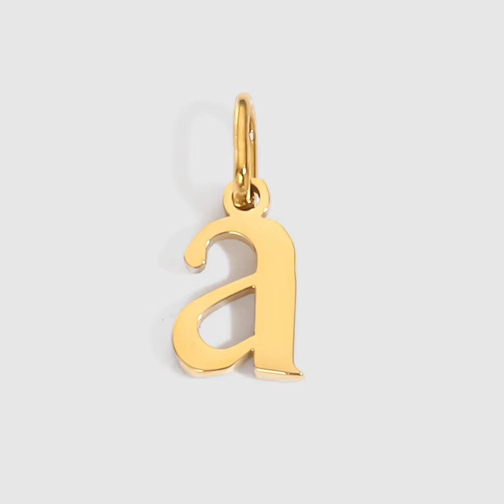 The Letter CHARM in lowercase a, a polished gold pendant in a serif a shape, shown in close-up on a light grey background.