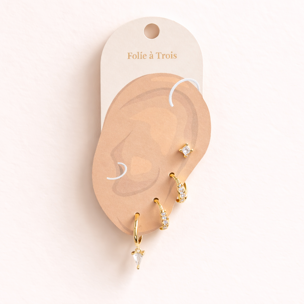 Lexi Set displayed on a Folie a Trois ear-shaped card in gold, arranging the stud and triangle crystal drop hoop for styling.