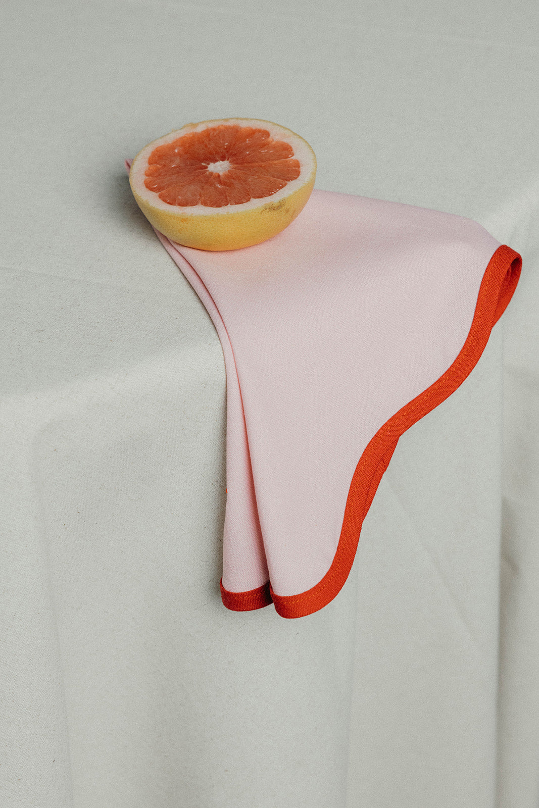 Orange Lilou Scallop napkin trimmed with a white scalloped edge, laid flat against a plain white background.