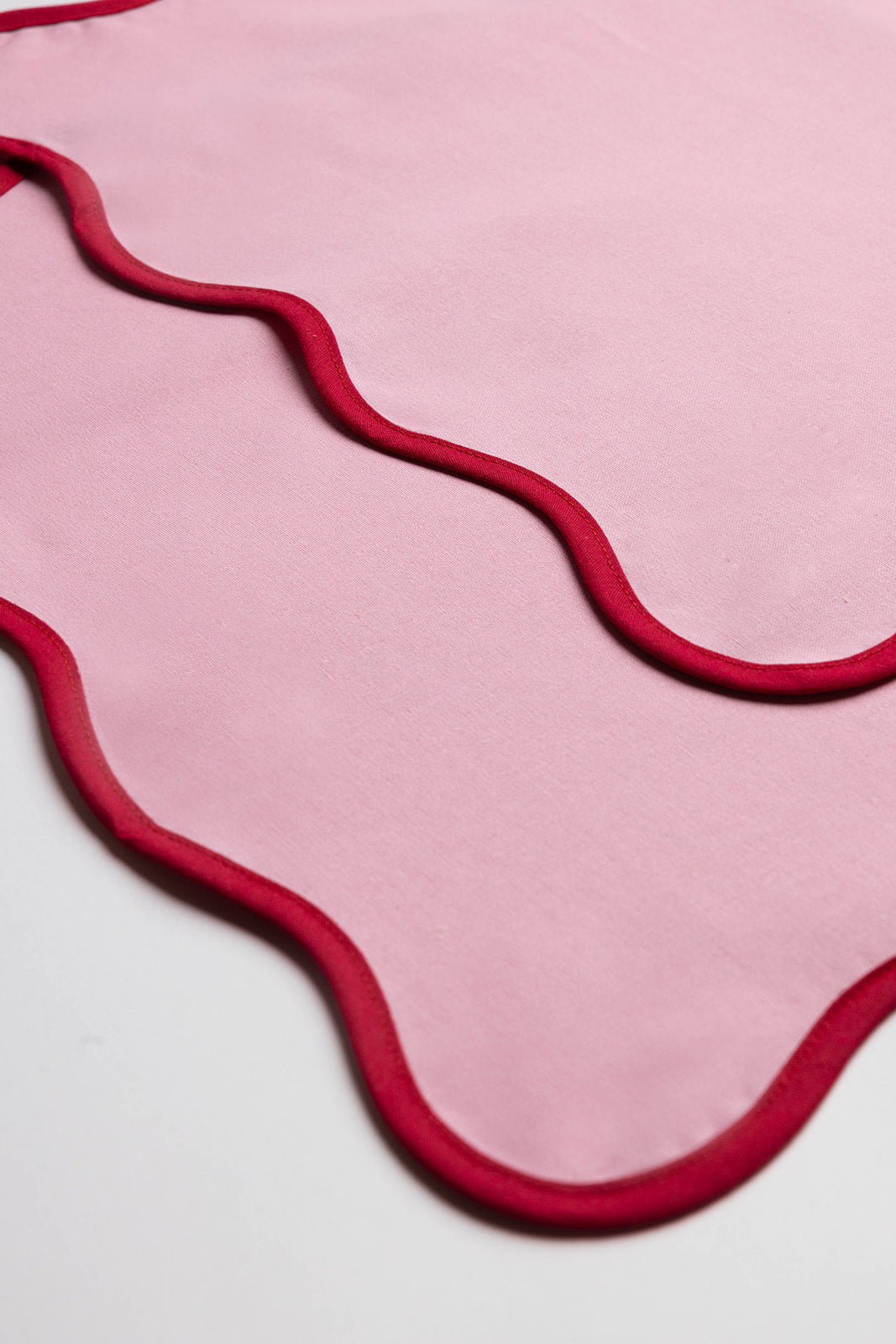 Close-up of the orange Lilou Scallop napkin's folded corner showing the crisp white scalloped trim detail.