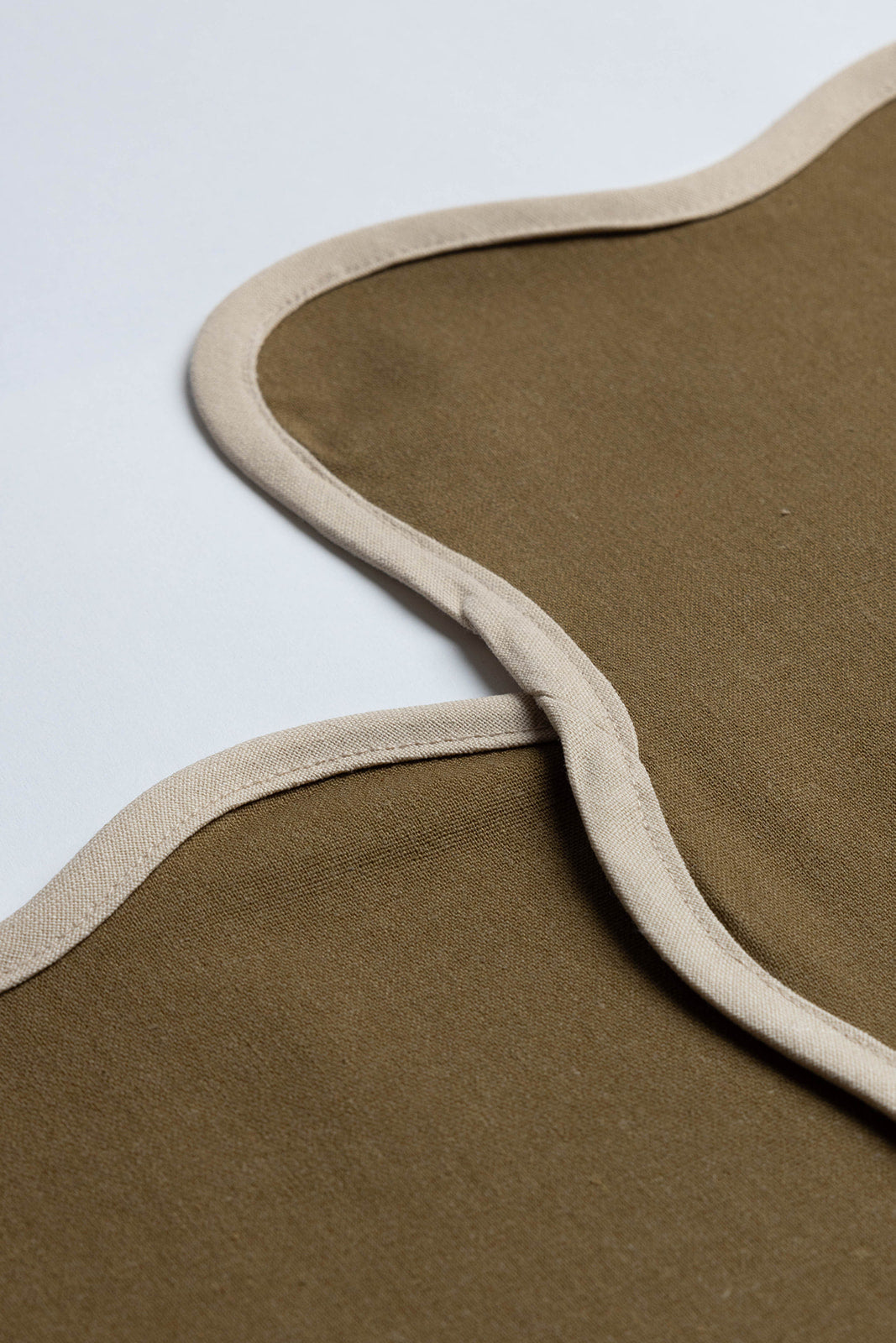 Close-up of two olive Lilou Scallop napkin edges meeting at a corner, highlighting the cream scalloped trim.