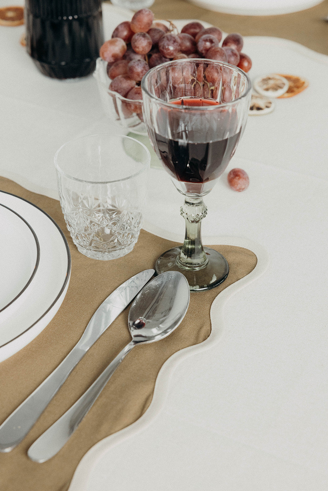 Close-up of the olive Lilou Scallop placemat corner beside a wine glass, water glass and polished cutlery on white linen.
