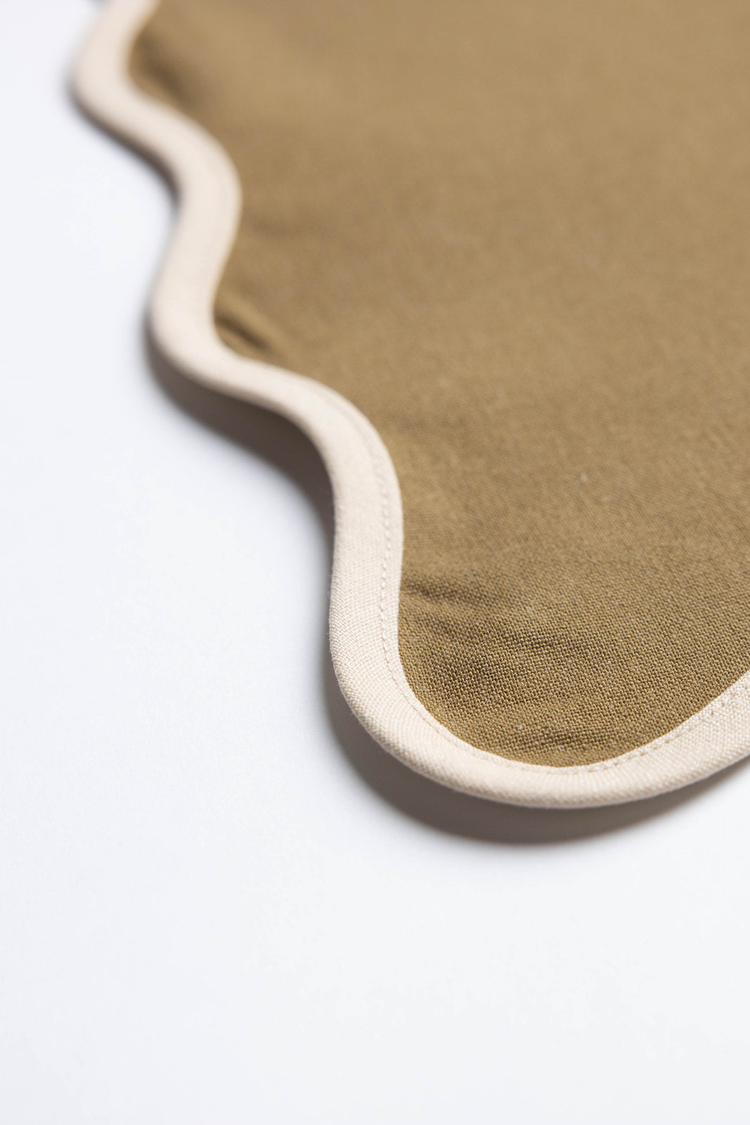 Macro shot of the pink Lilou Scallop placemat's scalloped edge, highlighting the contrasting red trim stitching detail.