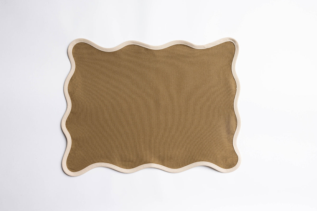 Ruffled Vive block-print cushions arranged on a wooden daybed frame set amid tall grass and wildflowers.