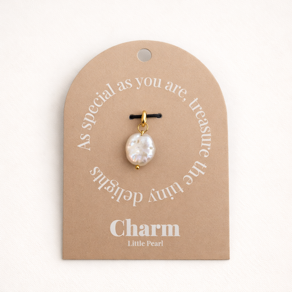 The Little Pearl CHARM displayed on a tan Charm gift tag, the round coin pearl pendant hanging from a black cord.
