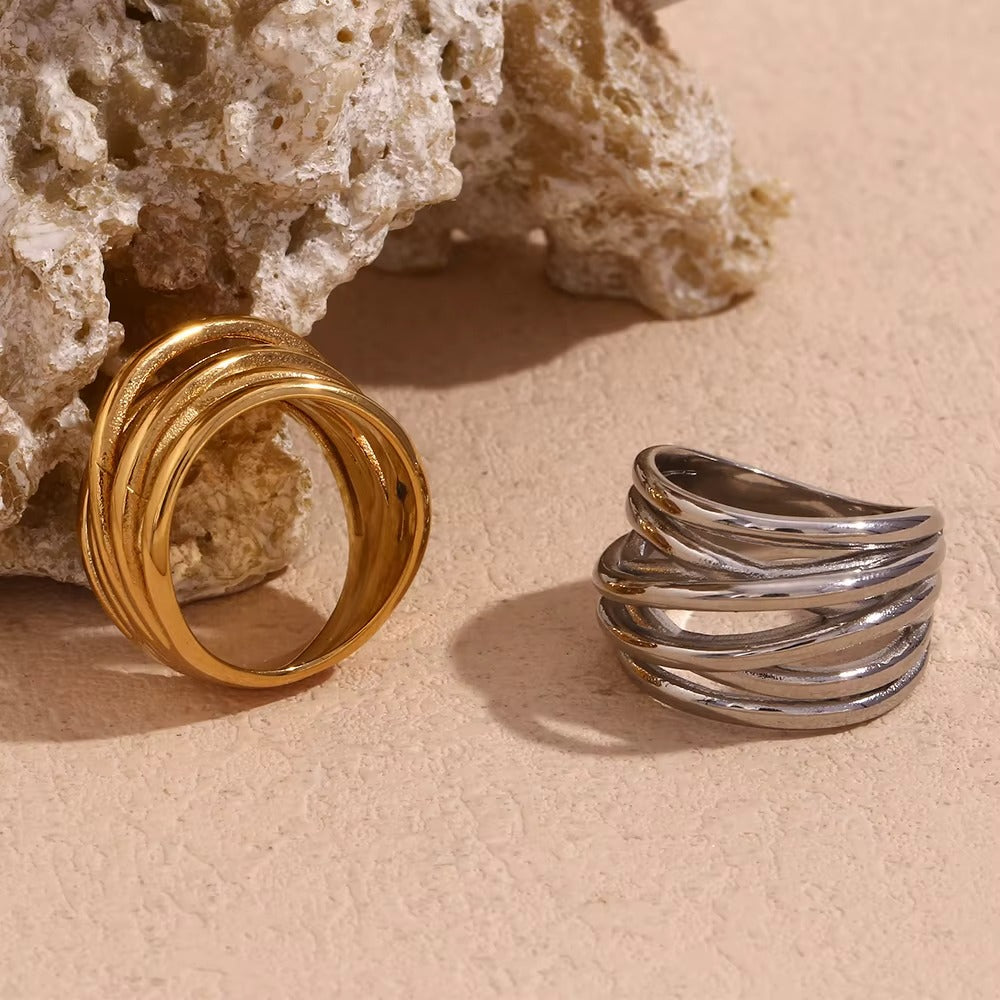 Gold and silver wide wrap-style Lizie RING pieces propped against a textured stone, layered wire bands visible.