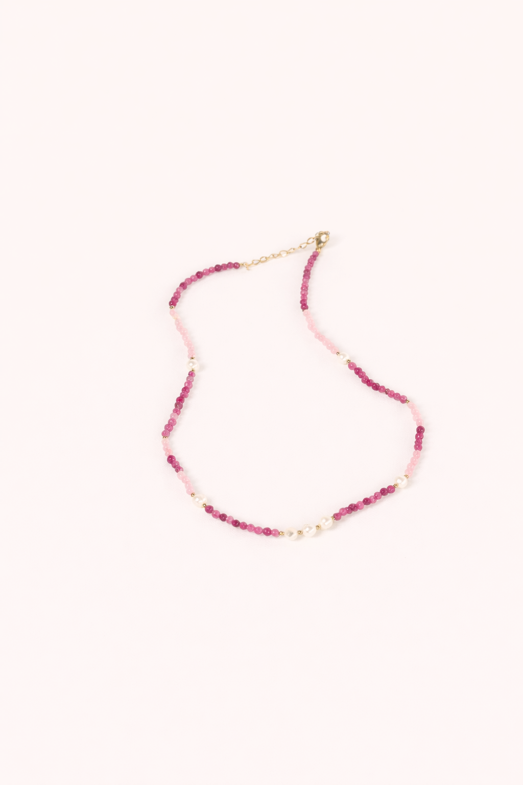 The Lolita NECKLACE, a beaded strand of pink and burgundy gemstones interspersed with small pearls, shown flat.