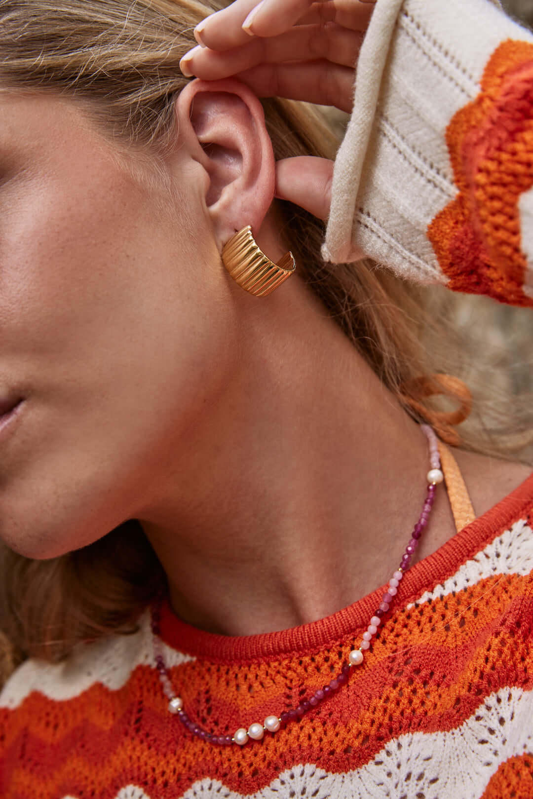 The Lolita NECKLACE worn at the neckline, pink and burgundy beaded strand with pearls against a knit striped sweater.