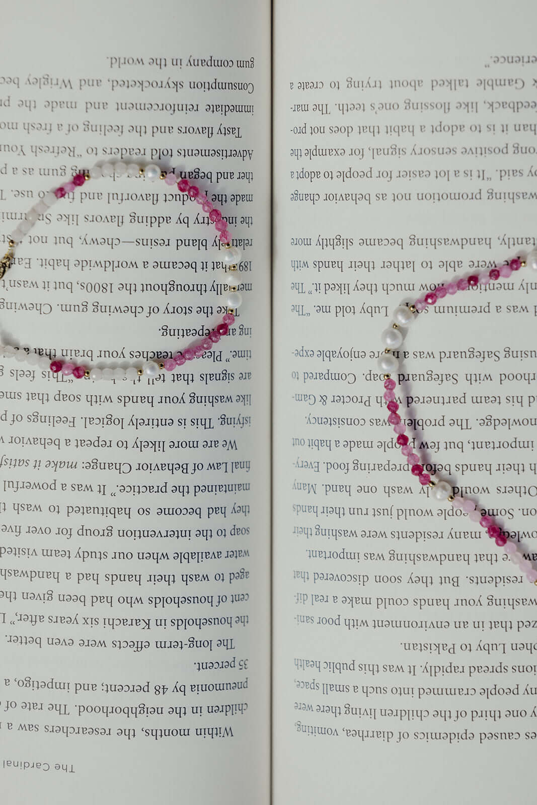 The Lolita NECKLACE in close-up, the pink and burgundy beaded strand with pearls draped across an open book.